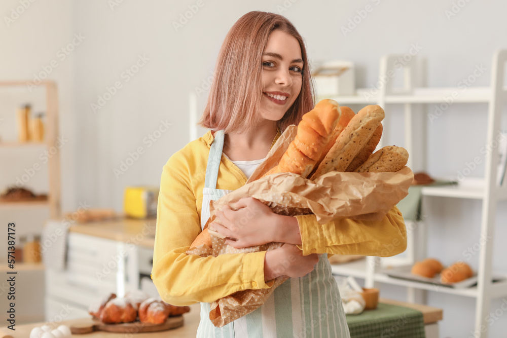 Female baker with fresh baguettes in kitchen