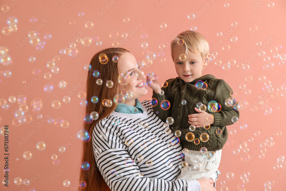 Happy mother with her little son and soap bubbles on pink background