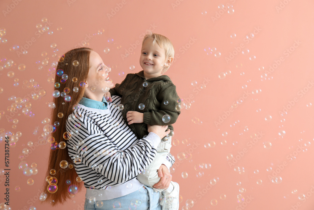 Happy mother with her little son and soap bubbles on pink background