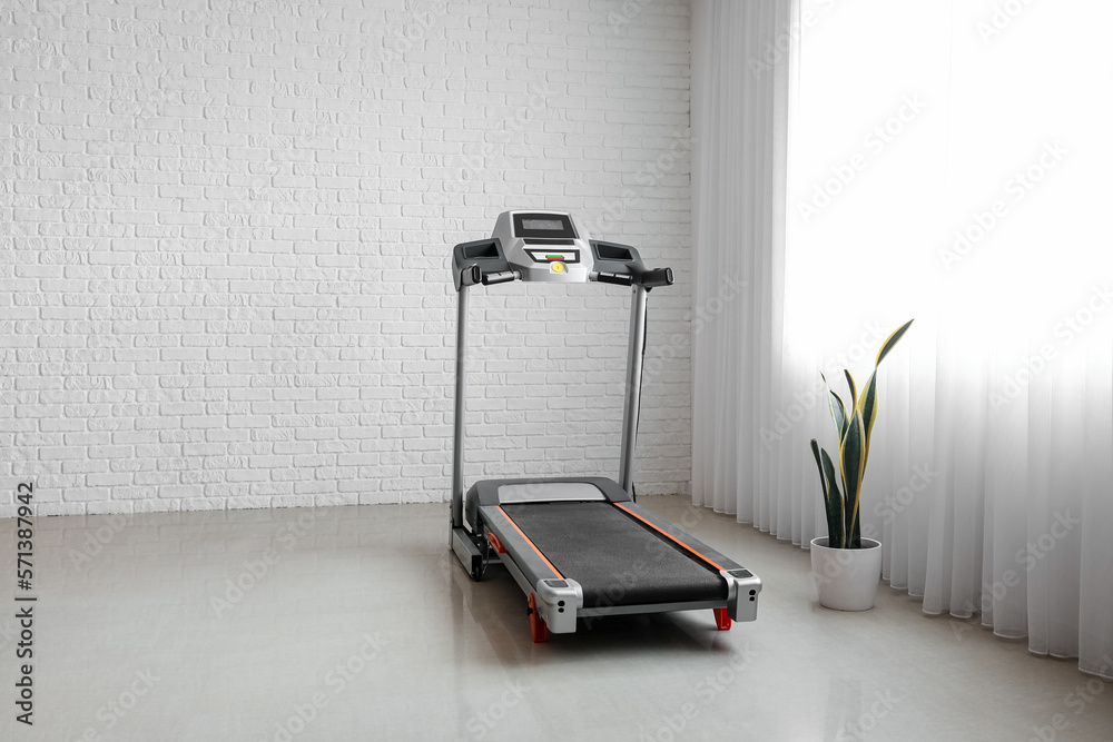 Interior of room with modern treadmill near grey wall