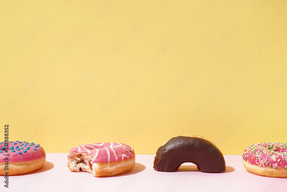 Different delicious donuts on pink table near yellow wall