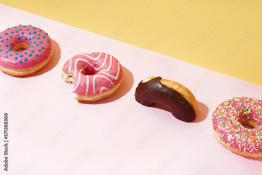 Different delicious donuts on pink table near yellow wall