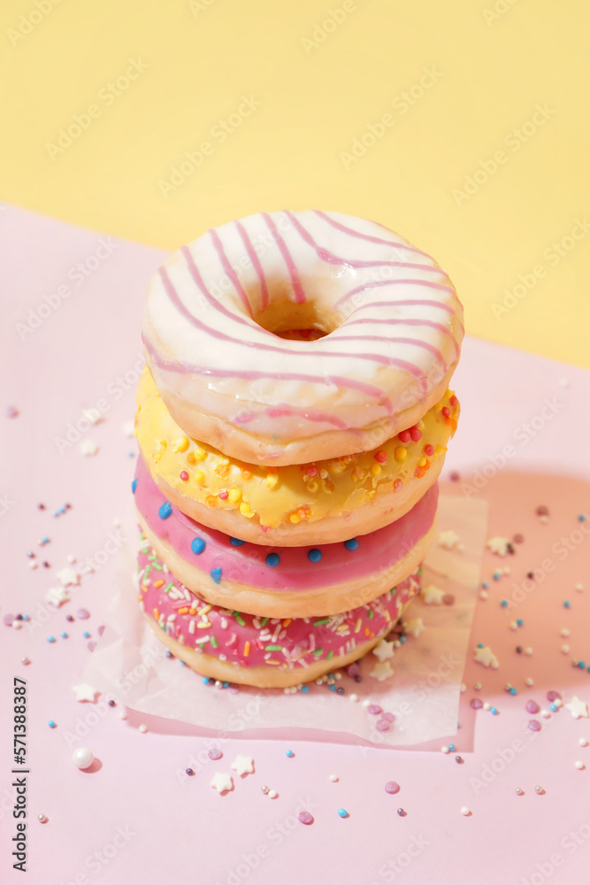 Parchment with different delicious donuts on pink table near yellow wall