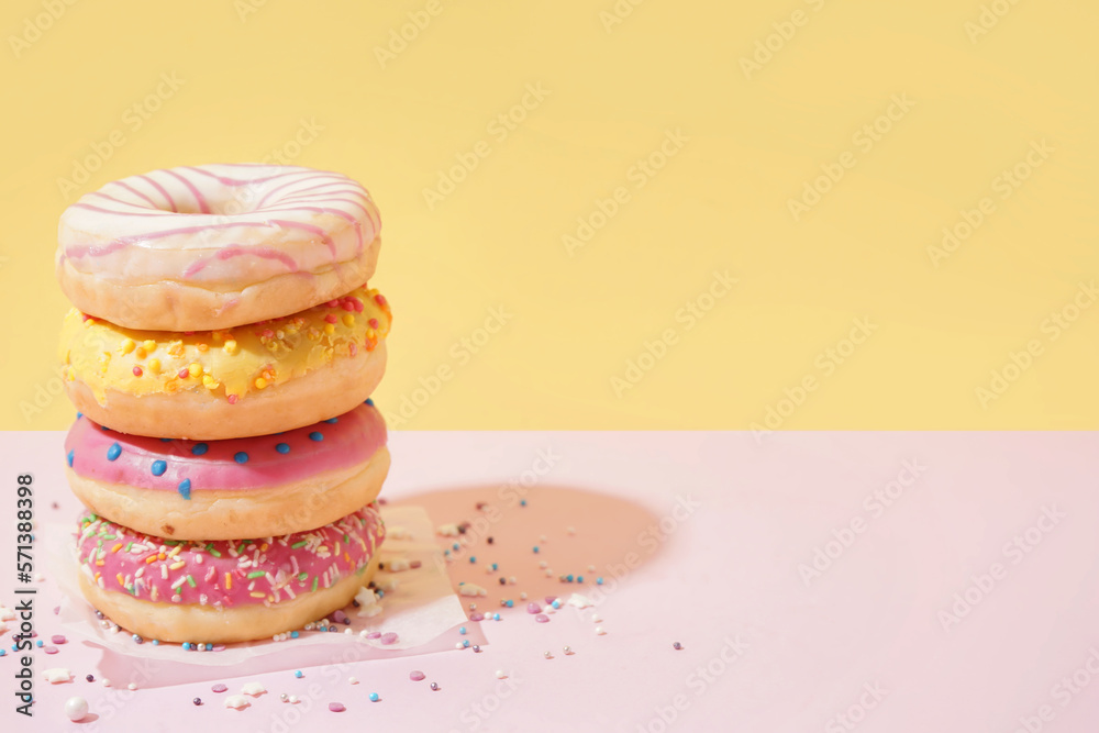 Parchment with different delicious donuts on pink table near yellow wall