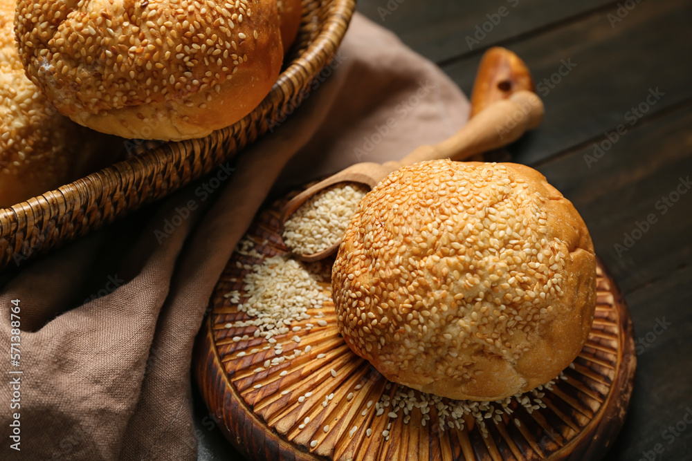 Board with delicious fresh bun and scoop of sesame seeds on black wooden table