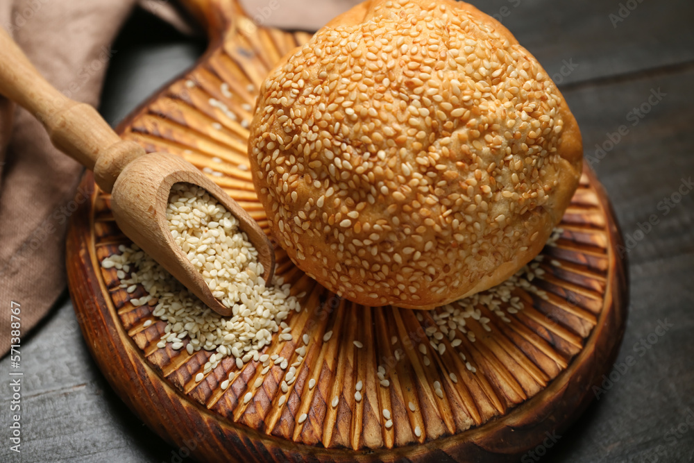 Board with delicious fresh bun and scoop of sesame seeds on black wooden table