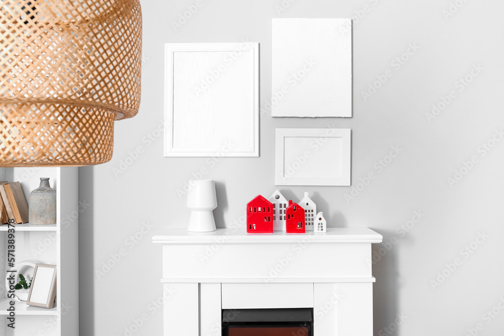 Interior of room with house candle holders on fireplace and blank frames near grey wall