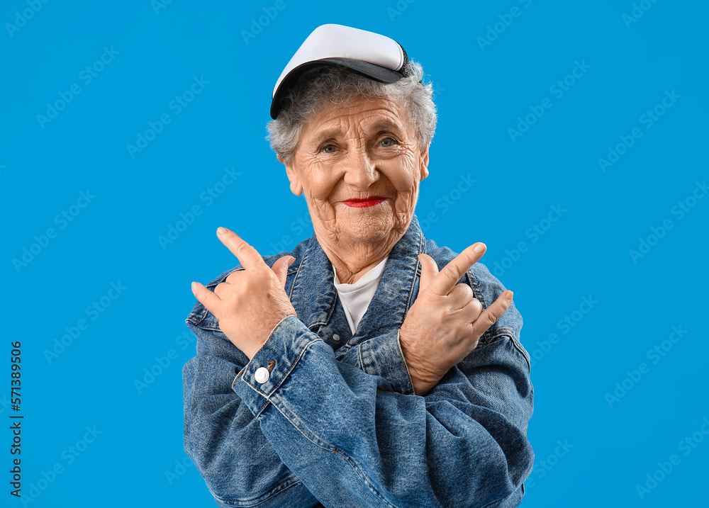 Senior woman in cap showing  i love you  gesture on blue background