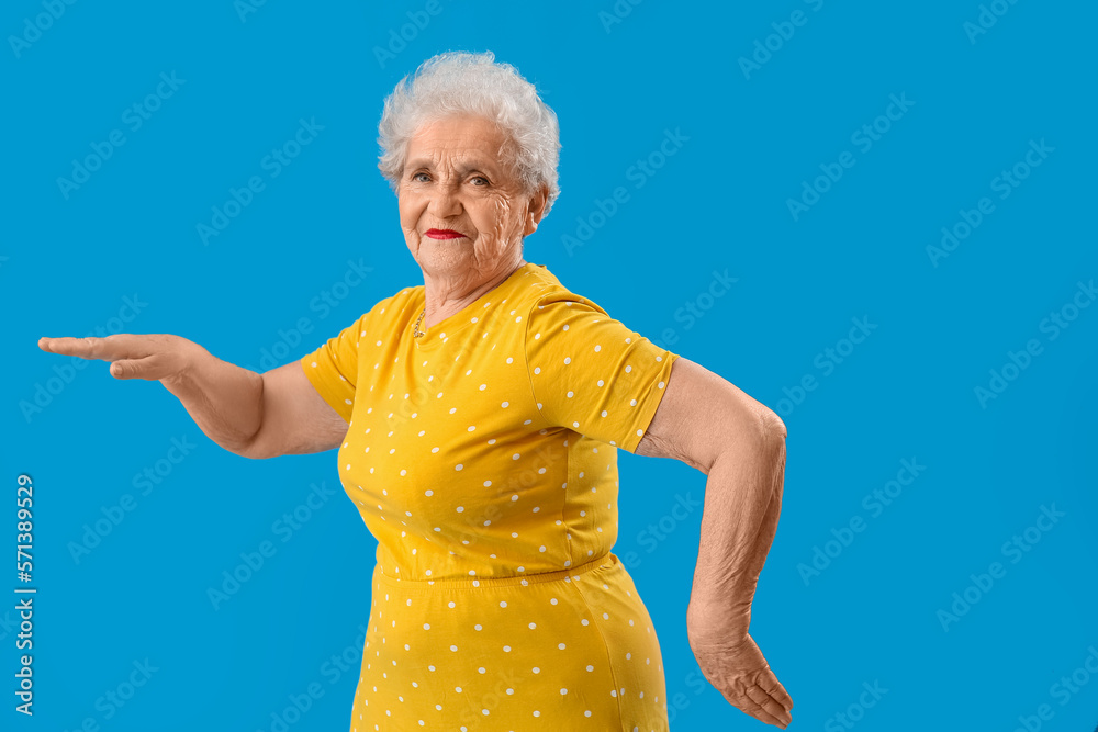 Senior woman in yellow t-shirt dancing on blue background