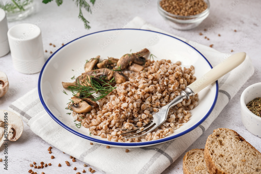 Plate of tasty buckwheat porridge with mushrooms and dill on grey table