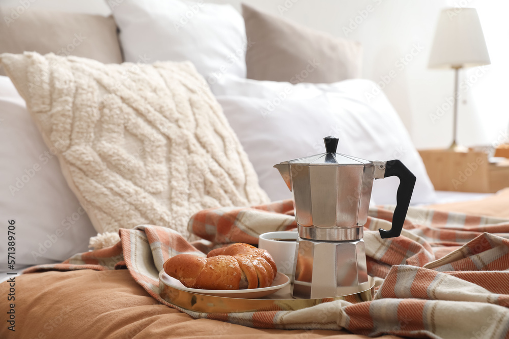 Plate with geyser coffee maker, delicious croissant and cup of espresso on bed