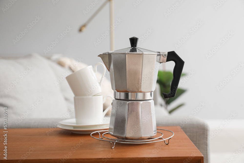 Grid with geyser coffee maker and cups on table in living room