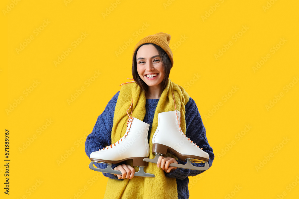 Pretty young woman with ice skates on yellow background