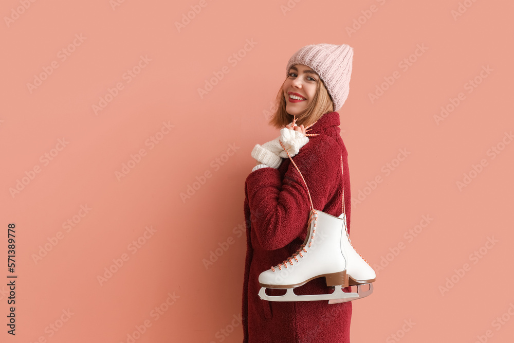 Pretty young woman with ice skates on pink background