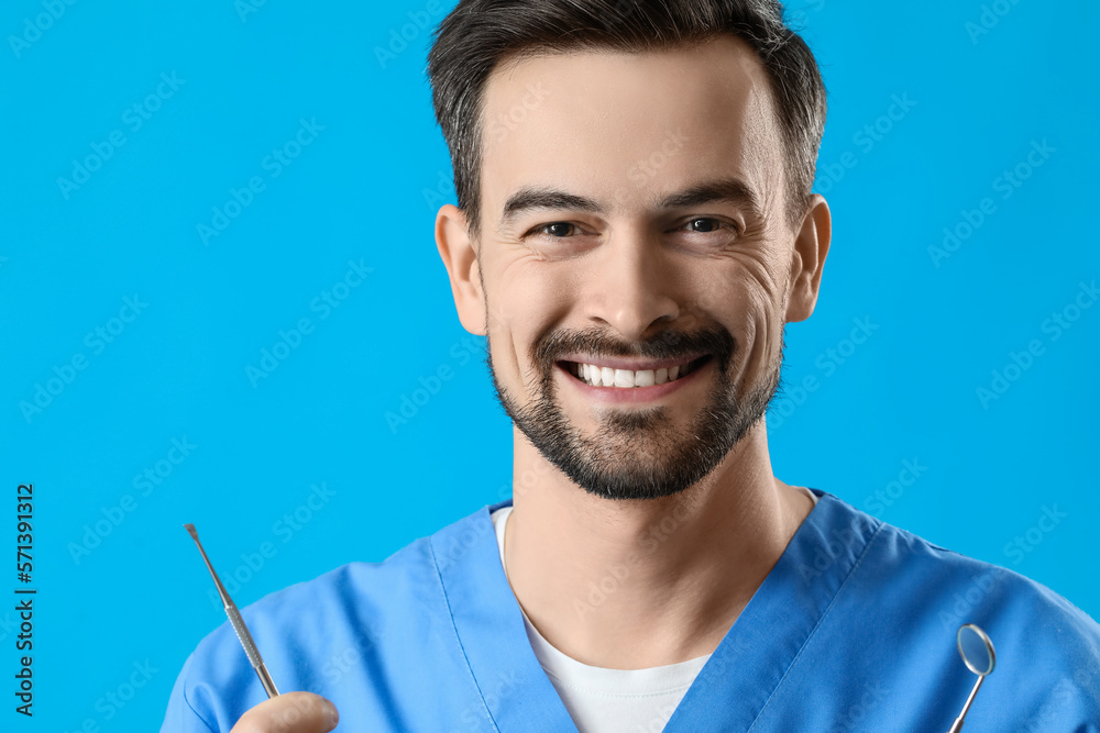 Smiling male dentist with tools on blue background, closeup