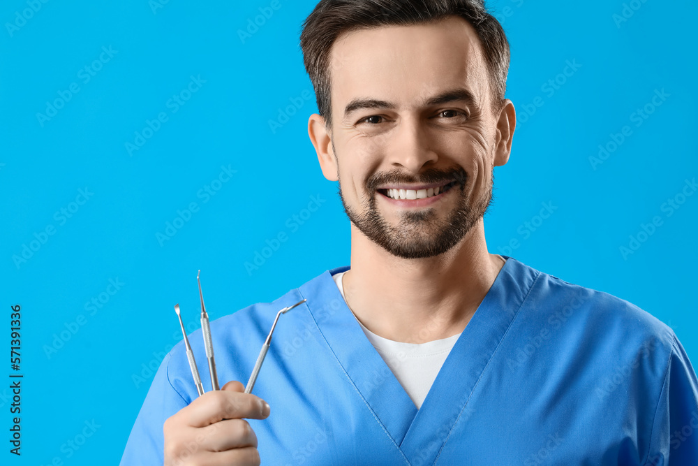 Smiling male dentist with tools on blue background, closeup