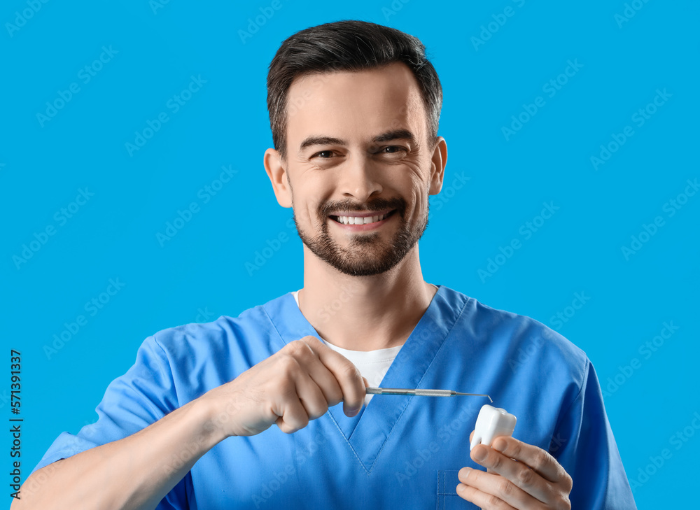 Male dentist with plastic tooth and tool on blue background, closeup