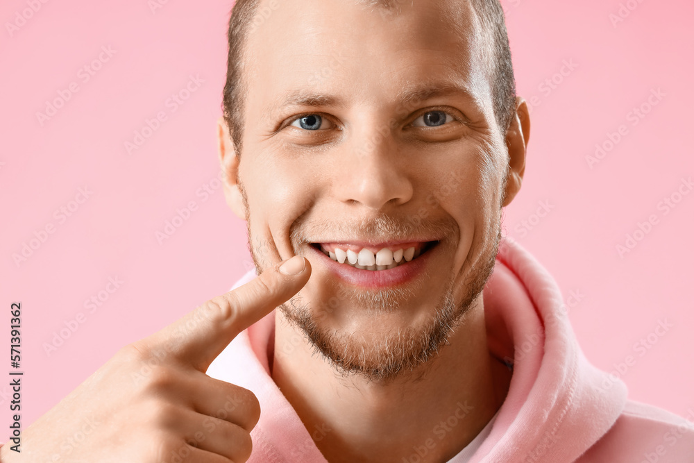 Young bearded man pointing at his teeth on pink background, closeup