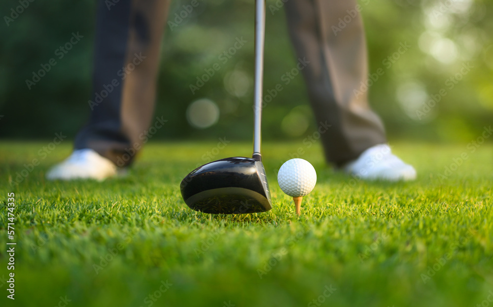 Close-up of golf ball on tee and drivers with golfer ready to tee off.