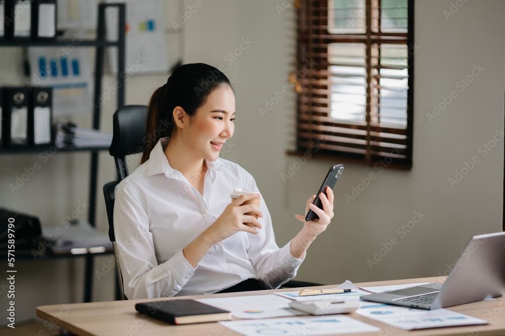 Business asian woman Talking on the phone and using a laptop with a smile while sitting at office..