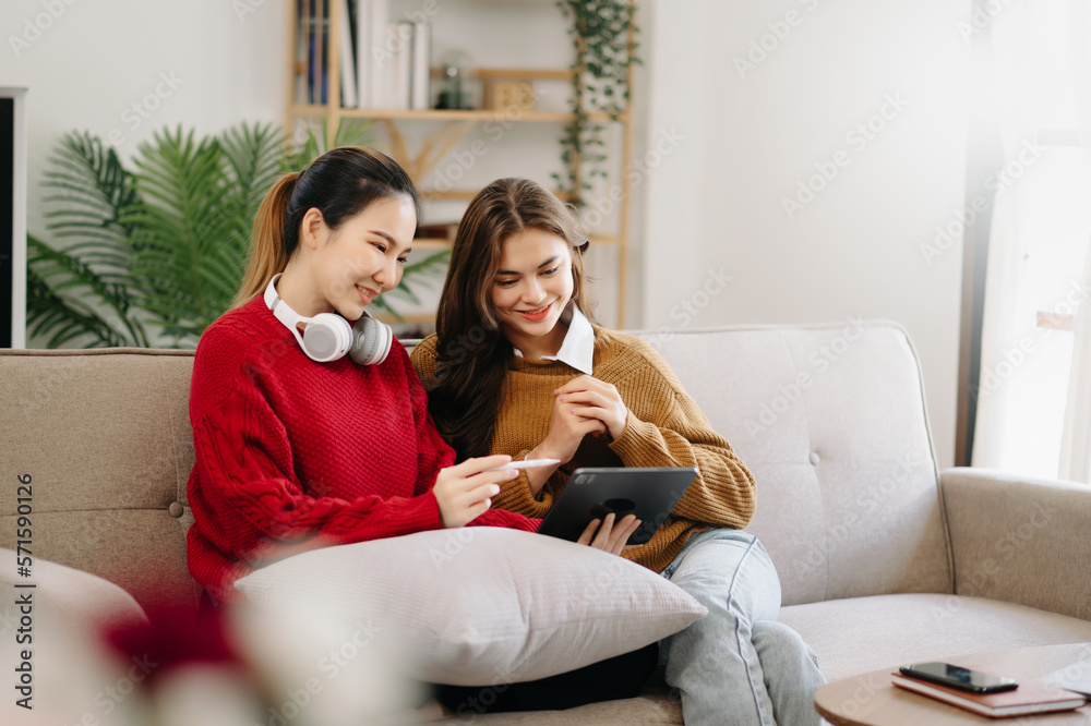 Two asian students learning together online with a laptop, tablet and tutor together in liveing room