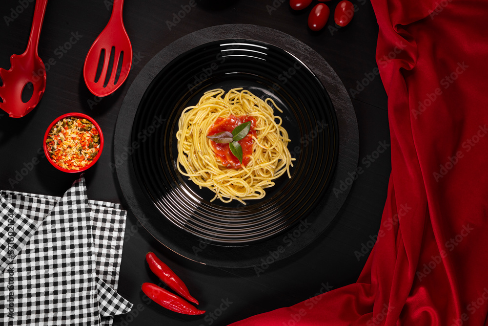 Spaghetti with sauce on a black plate in a darker studio photo.