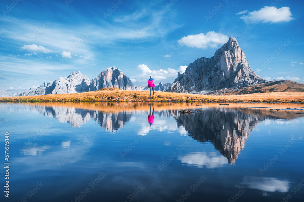 Woman and mountains reflected in lake at sunny day in autumn in Dolomites, Italy. Standing girl on t