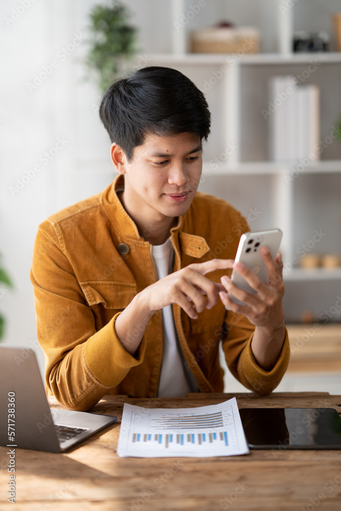 Portrait of young handsome Asian man using his asmartphone while working in comfortable office room.