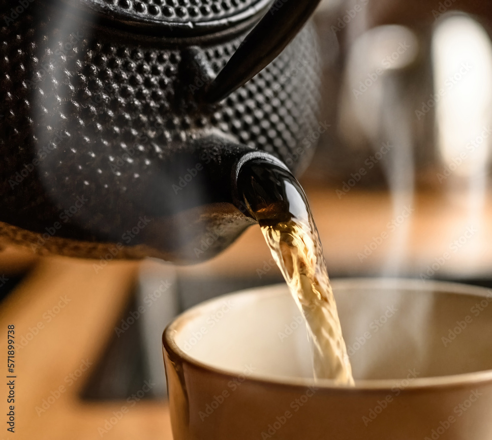 Pouring hot black tea from metal teapot at the kitchen close up. Steam comes out of the cup. Tea dri