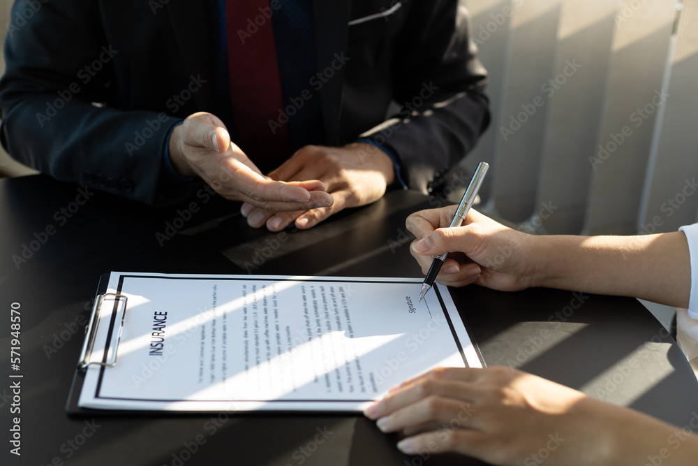 Businessman in suit in his office showing an insurance policy and pointing with a pen where the poli