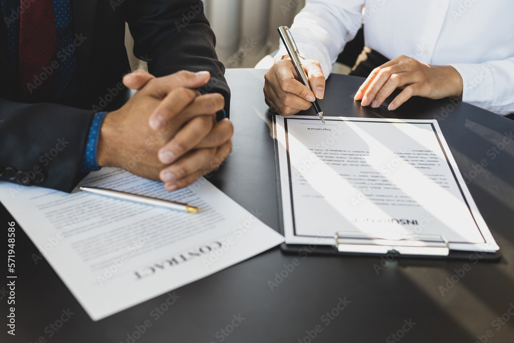 Businessman in suit in his office showing an insurance policy and pointing with a pen where the poli