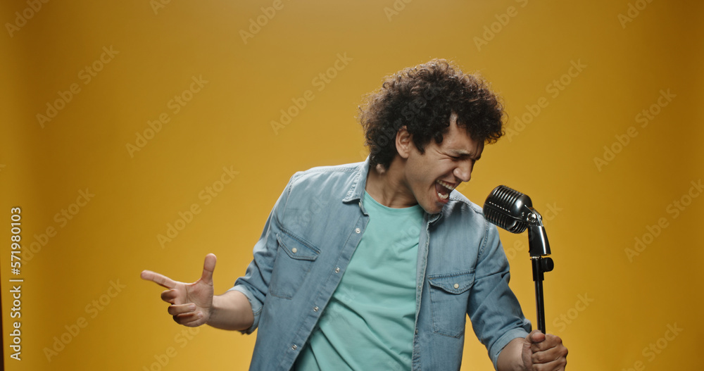 Close up shot of asian man with curly hair in casual clothes crazily dancing and singing in micropho