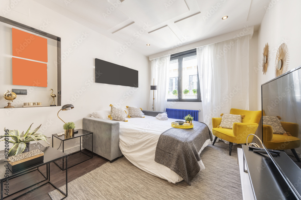 Living room of a house furnished with a sofa bed unfolded with a circular yellow tray under a window