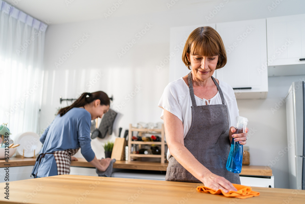 Caucasian senior elderly woman cleaning kitchen in house with daughter