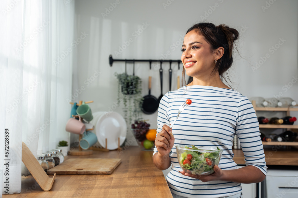 Caucasian young woman eating healthy green salad in kitchen at home. 