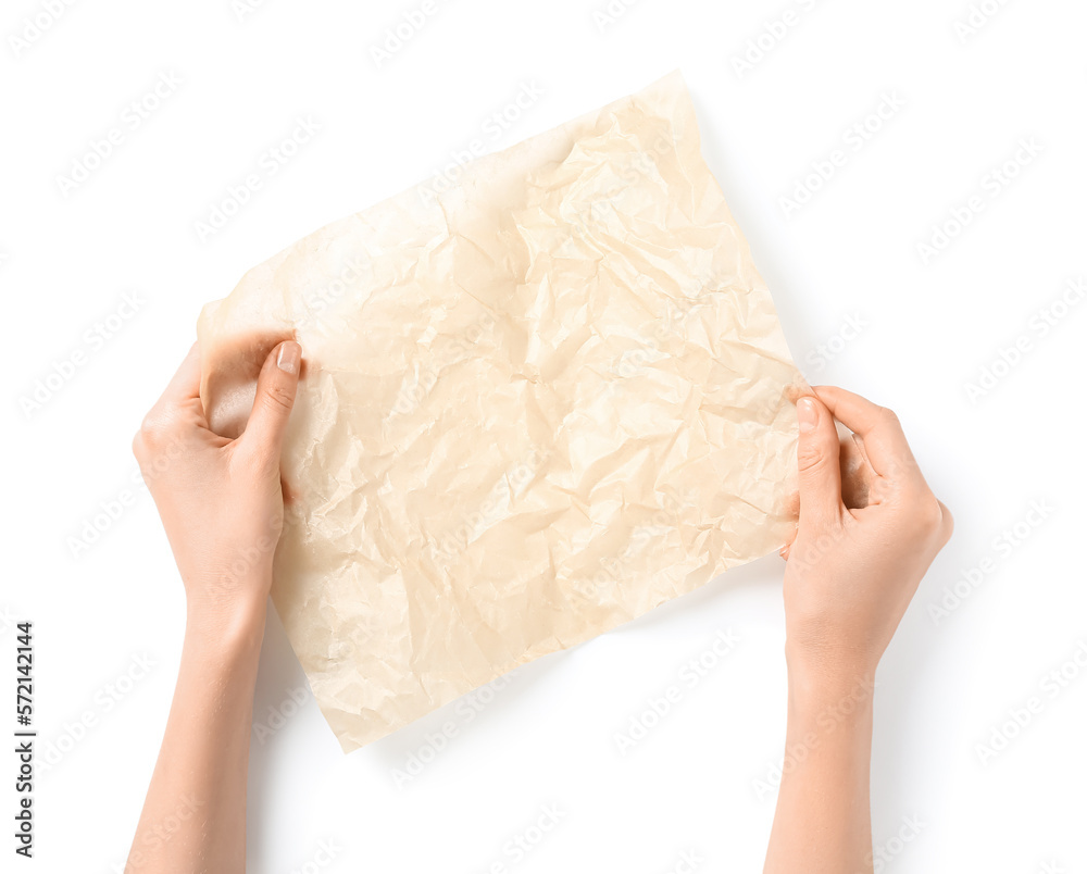 Female hands with sheet of crumpled baking paper on white background