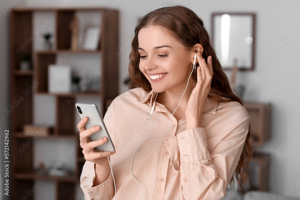 Young woman in earphones with mobile phone listening to music at home, closeup