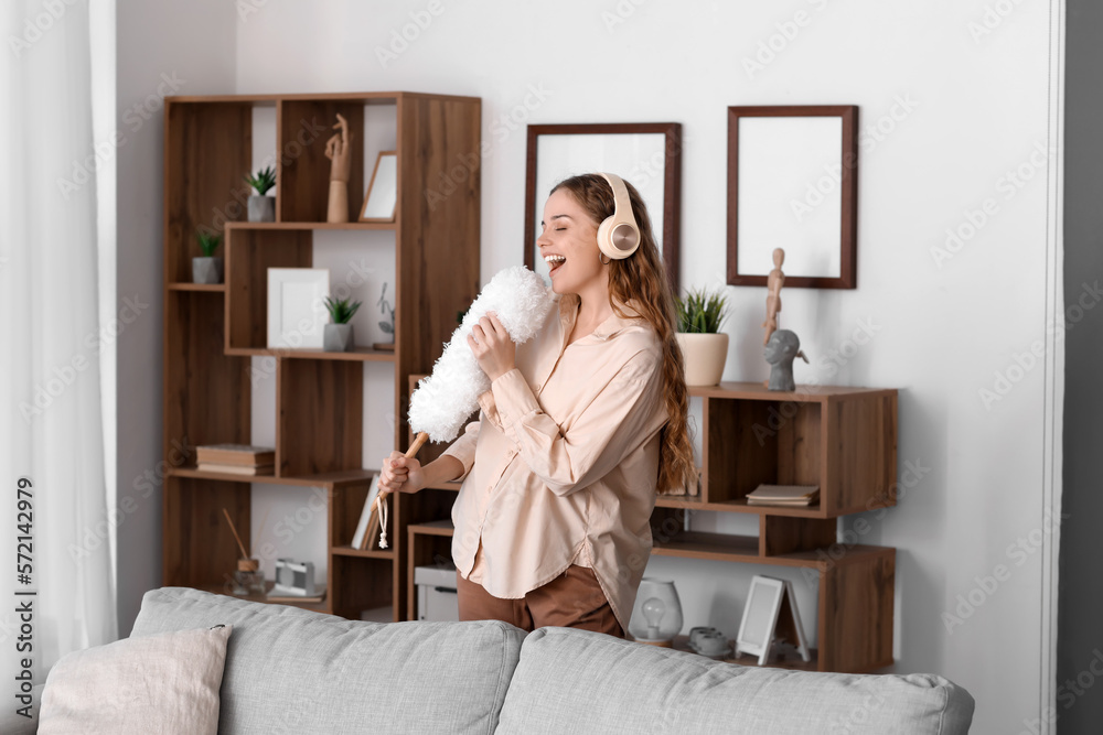 Young woman in headphones with duster singing at home