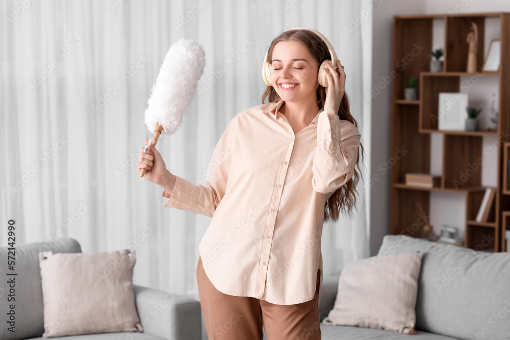 Young woman in headphones with duster listening to music at home