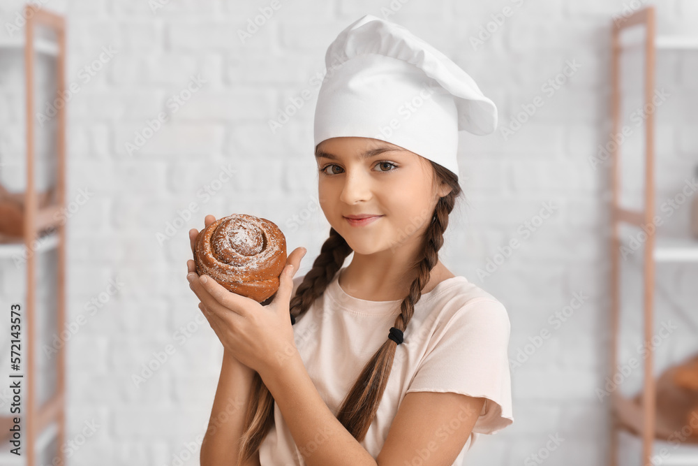 Little baker with tasty bun in kitchen, closeup