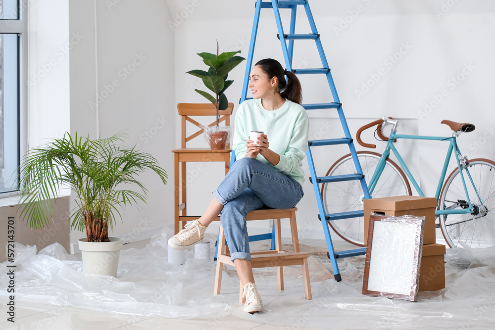 Young woman with paint can sitting on stepladder at home