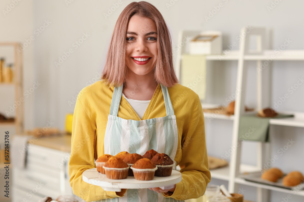 Female baker with tray of tasty cupcakes in kitchen