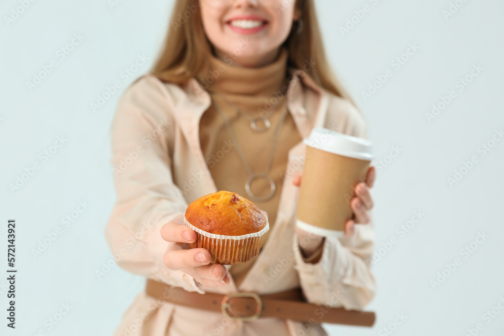 Young woman with tasty cupcake and cup of coffee on light background, closeup