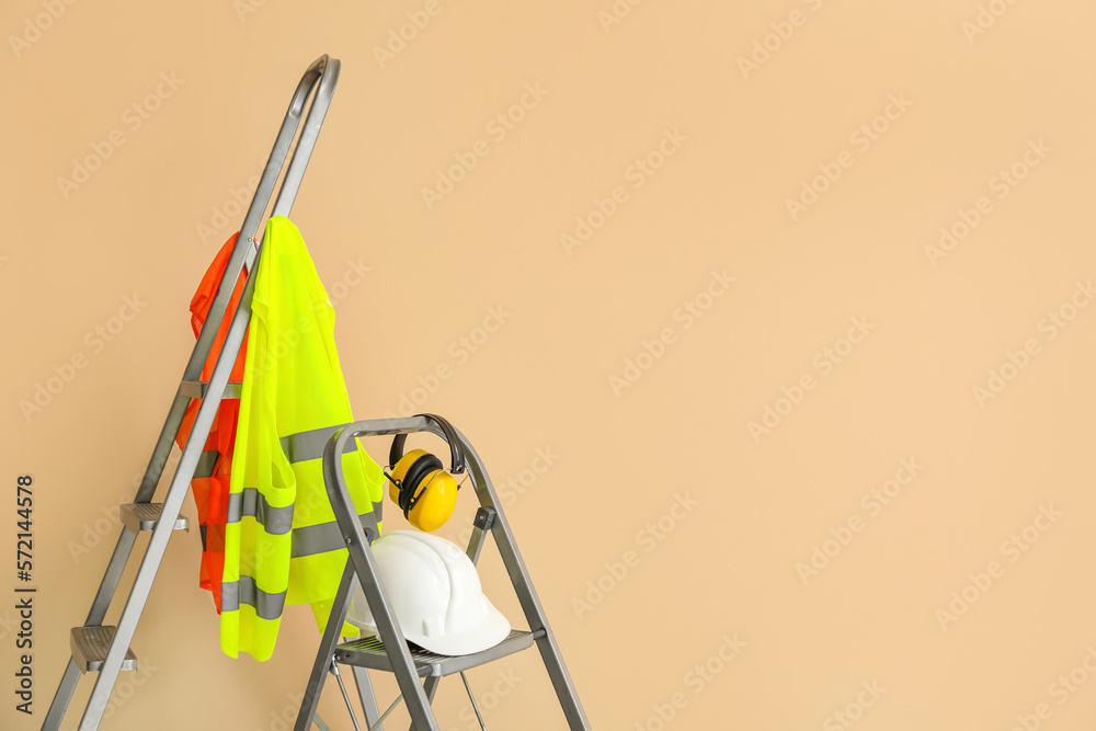 Stepladders with builders equipment and reflective vests near beige wall