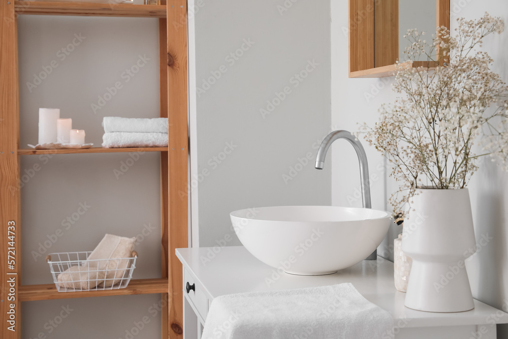 Sink and vase with flowers on table in light bathroom