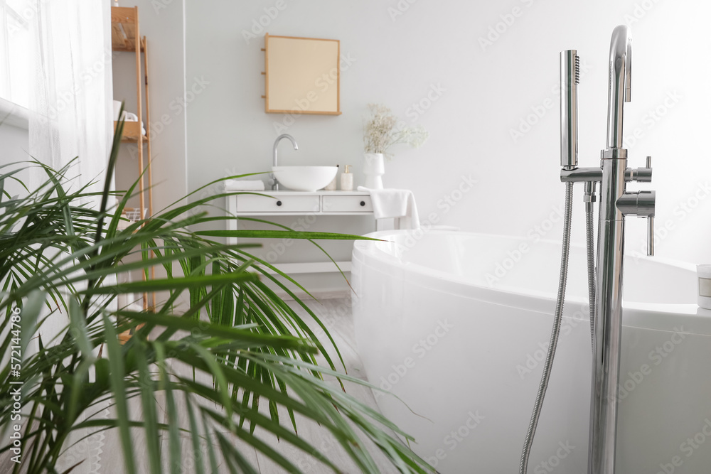 Interior of light bathroom with bathtub, table and sink