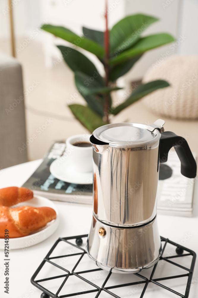 Grid with geyser coffee maker, cup of espresso and delicious croissant on table in living room