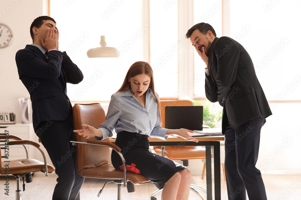 Young men playing a prank with whoopee cushion on their colleague in office. April Fools Day celebr