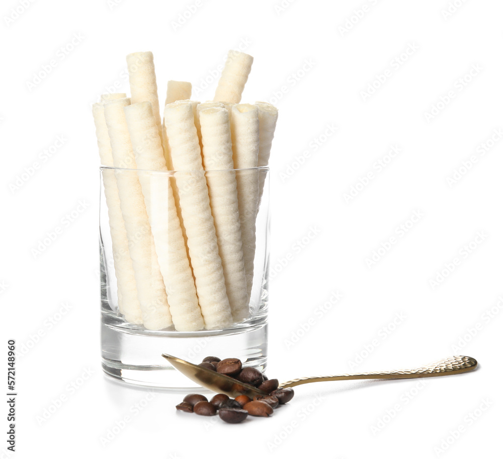 Glass with delicious wafer rolls  and spoon of coffee beans isolated on white background