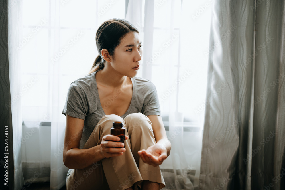  woman sit Depression Dark haired  pensive glance Standing with glass of water and pills by window a